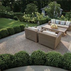 an outdoor living area with couches and tables surrounded by greenery in front of a house