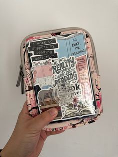 a person holding up a small zippered bag with stickers on it's side