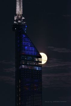 the moon is setting behind a tall building