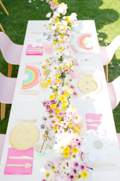 a long table with flowers and plates on it in the middle of a grassy area