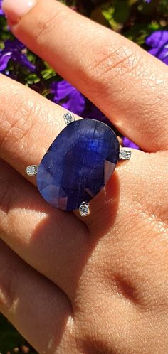 a woman's hand with a blue ring on it and purple flowers in the background