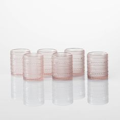 four pink glass tumblers lined up on a reflective surface