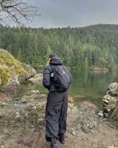 a man standing on top of a rocky hillside next to a lake with trees in the background