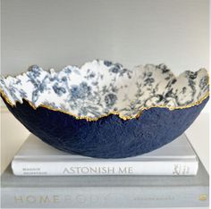 a blue and white bowl sitting on top of a book next to a stack of books