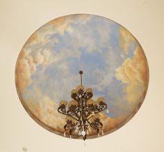 an ornate chandelier hanging from the ceiling with clouds in the sky behind it