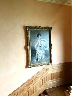 an old painting hangs on the wall next to a stair case in a room with wooden floors