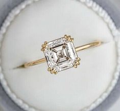 an engagement ring with a square cut diamond in the center on a white cloth background