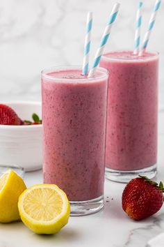 two glasses filled with smoothie next to strawberries and lemons