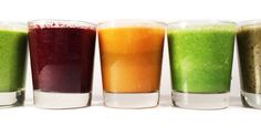 four glasses filled with different colored liquids sitting next to each other on a white surface