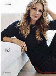 a woman sitting on top of a white couch next to a wall with her hand on her head