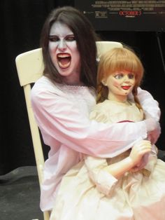 a creepy doll sitting on top of a chair next to a woman in a white dress