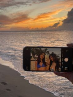 a person holding up a cell phone to take a photo on the beach at sunset