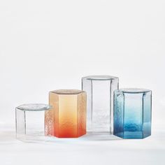 four different colored glass vases sitting next to each other on a white tablecloth