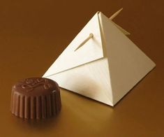 an origami pyramid next to a piece of chocolate