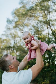 a man holding up a baby in the air with trees in the back ground behind him