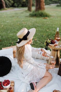 a woman sitting on top of a blanket holding a glass of wine