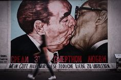 a man walking past a large painting of two men kissing each other