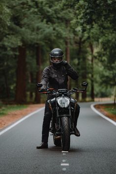 a man riding on the back of a motorcycle down a road in front of trees