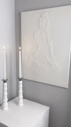 two candles sitting on top of a white table next to a painting and candle holder