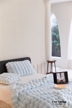 the bed is made up with fluffy blue blankets and pillows on it, along with a tablet computer