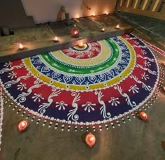 a colorfully decorated floor with lit candles around it and an artistic design on the ground