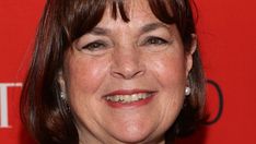 a close up of a person wearing a necklace and smiling at the camera with a red background