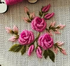 some pink flowers are sitting on a white table cloth next to two spools of thread