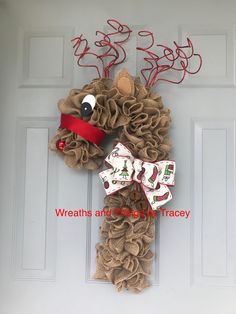 a christmas wreath hanging on the front door with reindeer head and red ribbon tied to it