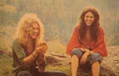 two women sitting next to each other in front of a rock and grass covered field