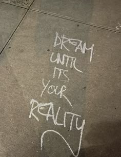 graffiti written on the sidewalk says dream until it's your reality with white spray paint