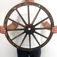 a man holding a wooden wheel in front of his face and wearing a white t - shirt