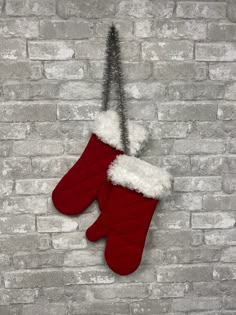 a pair of red mittens hanging from a brick wall with snow on the bottom