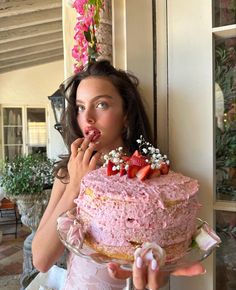 a woman is holding a large cake with strawberries on it and eating the cake