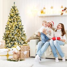 two women and a baby sitting on a couch with presents in front of a christmas tree