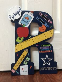 a wooden letter shaped like the letter e with school supplies on it and a ruler