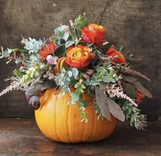 a pumpkin filled with flowers and greenery on top of a wooden table next to a wall