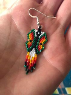 a hand holding a pair of colorful beaded earrings in it's palm area