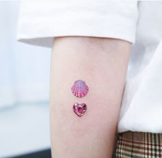 a small pink shell and heart tattoo on the left arm, with two smaller hearts