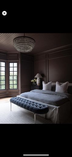 a large bed sitting in the middle of a bedroom next to two windows with chandeliers