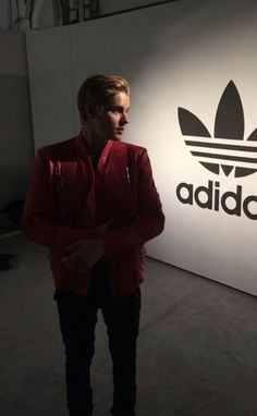 a man standing in front of a wall with the adidas logo on it's side