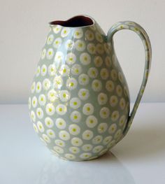 a green and white vase with yellow flowers on the inside is sitting on a table