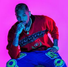 a man sitting on top of a stool wearing blue pants and a red shirt with tattoos