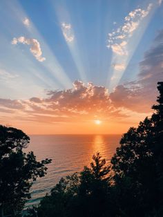 the sun is setting over the ocean and trees