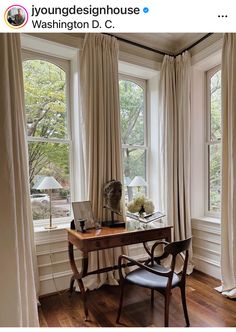 a desk with a laptop on top of it in front of two windows and curtains