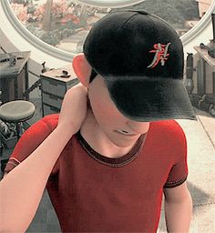 a boy in a red shirt and black hat is looking at his cell phone while wearing a baseball cap