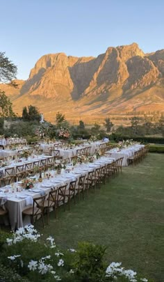 a long table is set up in the middle of a field with mountains in the background