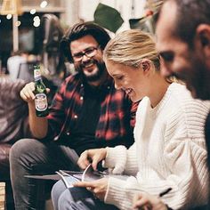 two men and a woman sitting next to each other on couches with beer in hand