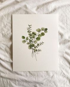 a card with green leaves on it sitting on a white sheet in the middle of a bed