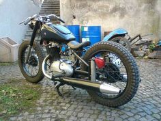 the motorcycle is parked on the cobblestone road near an old building and blue water tank