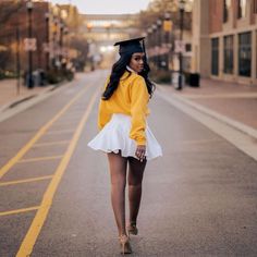 a woman walking down the street wearing a graduation cap and white miniskirt with high heels